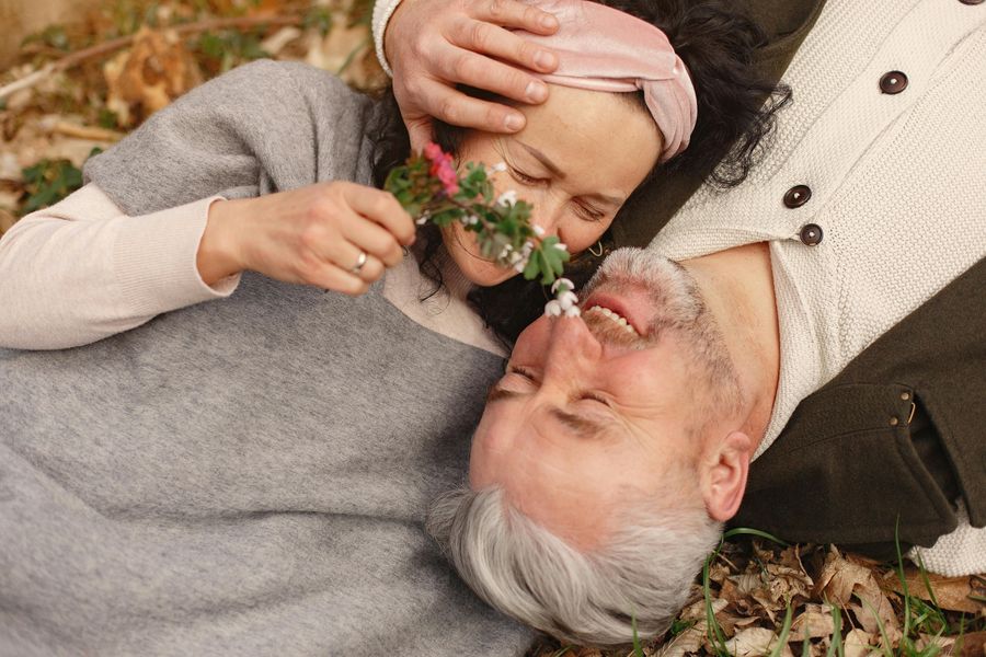 Pareja sénior sonriente tumbada sobre hojas de otoño con unas flores